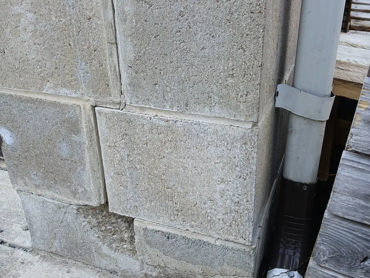 A cut stone block wall with an open joint running through the courses beside a downspout