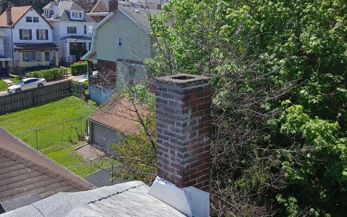 A brick chimney standing above a shingle roof with the neighbourhood behind it
