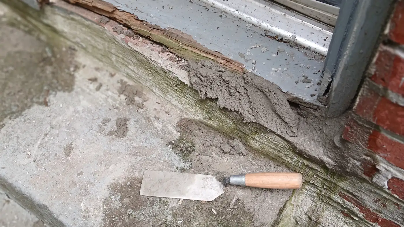A pointing trowel resting on a stone sill part way through a repair